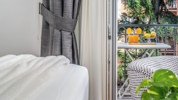 Habitación de hotel con cama, balcón con mesa y vistas a zonas verdes.