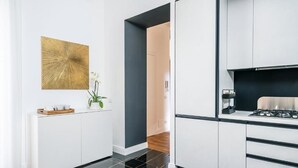 Una cocina moderna con armarios blancos, piso de baldosas negras y una obra de arte abstracta dorada en la pared.