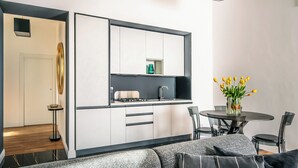 Una cocina compacta con armarios blancos, encimera negra y un pequeño comedor con mesa y sillas.