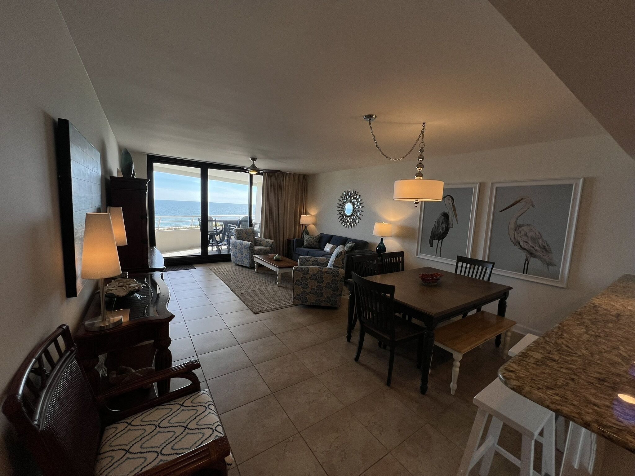 A spacious living area with a balcony overlooking the sea, furnished with a sofa, chairs, and a dining table.