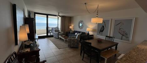 A spacious living area with a balcony overlooking the sea, furnished with a sofa, chairs, and a dining table.