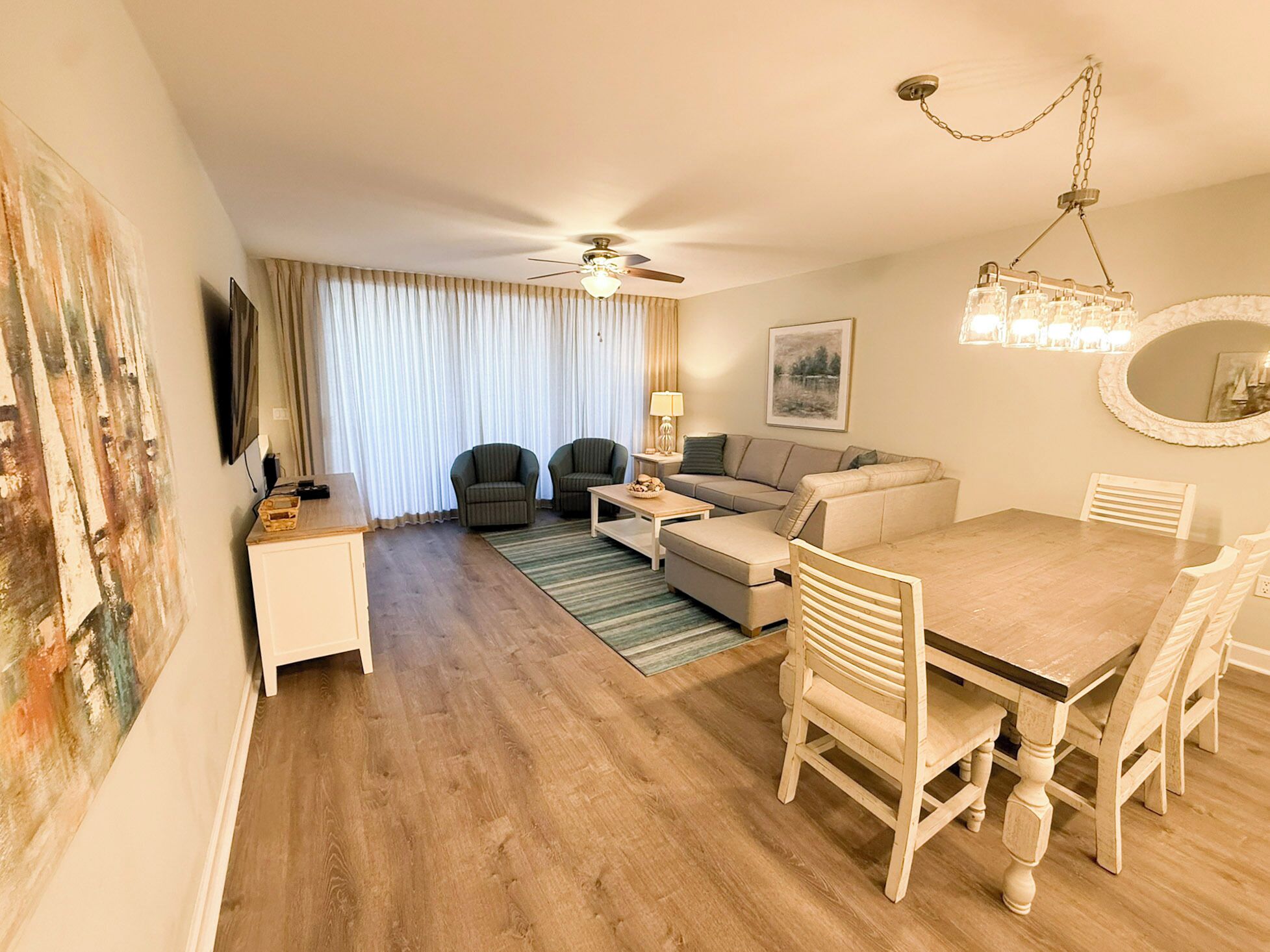 Ein Wohnzimmer mit einer Couch, Sesseln, einem Esstisch, einem Deckenventilator und einem Fernseher.