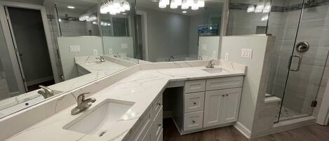 A modern bathroom with a large mirror, two sinks, a shower, and a walk-in shower.