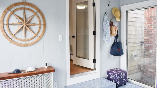 Een kamer met een houten bankje, een decoratieve ster aan de muur, een deur naar een badkamer en een klein krukje.