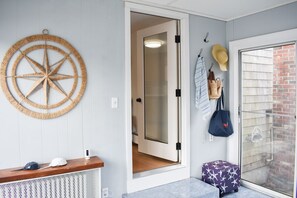 Une pièce comprenant un banc en bois, un élément décoratif mural en forme d’étoile, une porte donnant sur une salle de bain et un petit tabouret.
