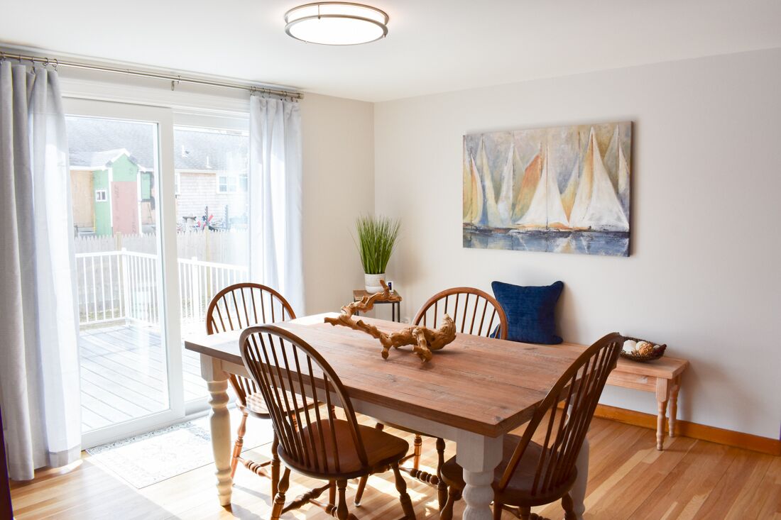 A dining area with a wooden table and chairs, a potted plant, and a sailboat painting on the wall.
