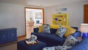 Een woonkamer met een blauwe bank, gele en blauwe kussens, een houten bijzettafeltje en een geel boekenkast.