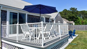 Een overdekt terras met een witte reling, een blauwe parasol en twee blauwe Adirondack-stoelen.