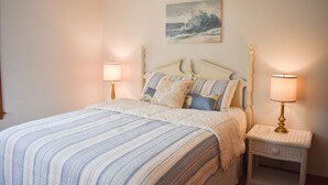 Een slaapkamer met een bed, twee bedlampjes, een schilderij van een golf en een witte nachtkastje.