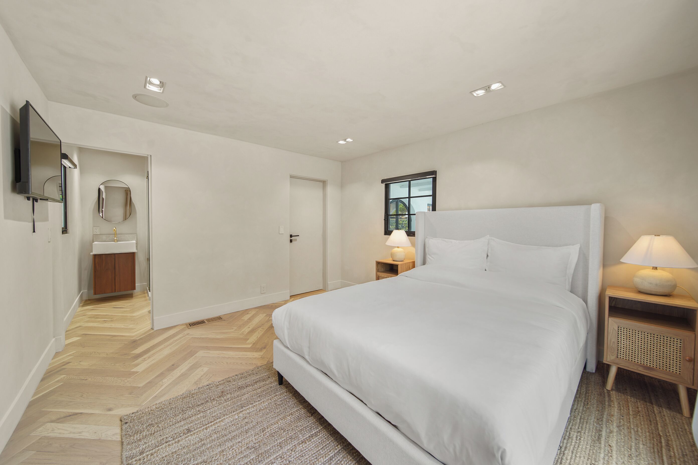Een moderne slaapkamer met een groot bed, nachtkastjes, een spiegel en een raam.