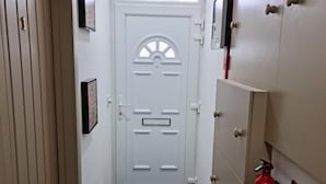 A narrow hallway with a white door featuring a decorative glass panel and a black mail slot. There are two fire extinguishers mounted on the wall to the right. - Surebillionaire Home Deluxe Queen Studio (London)