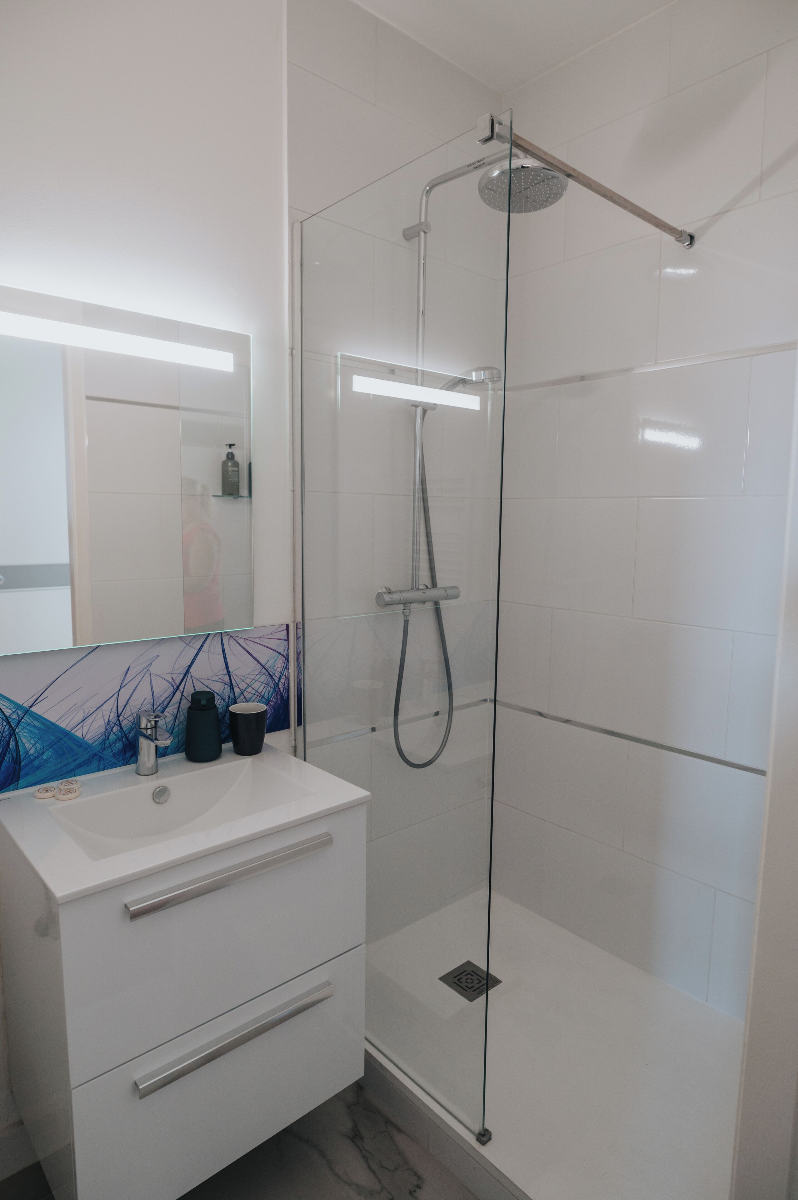A modern bathroom with a glass-enclosed shower, a white sink with a glass backsplash, and a mirror above the sink.