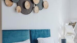 A neatly arranged bed with white and teal pillows, a teal upholstered headboard, and a wall-mounted decorative arrangement. - Le Rêve Bleu (Thionville)