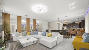A modern living room with a sectional sofa, a yellow armchair, and a dining area with a kitchen in the background.