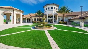 A courtyard with a central fountain, surrounded by buildings with arched walkways and palm trees.
