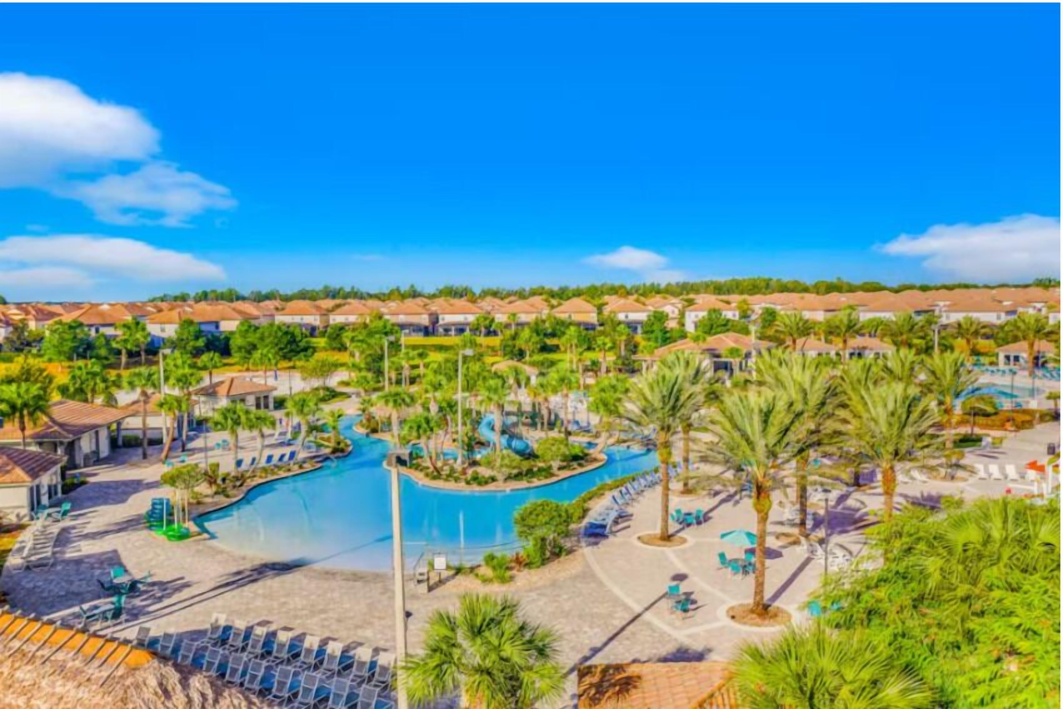 Un resort con una amplia piscina, palmeras y un cielo azul despejado.