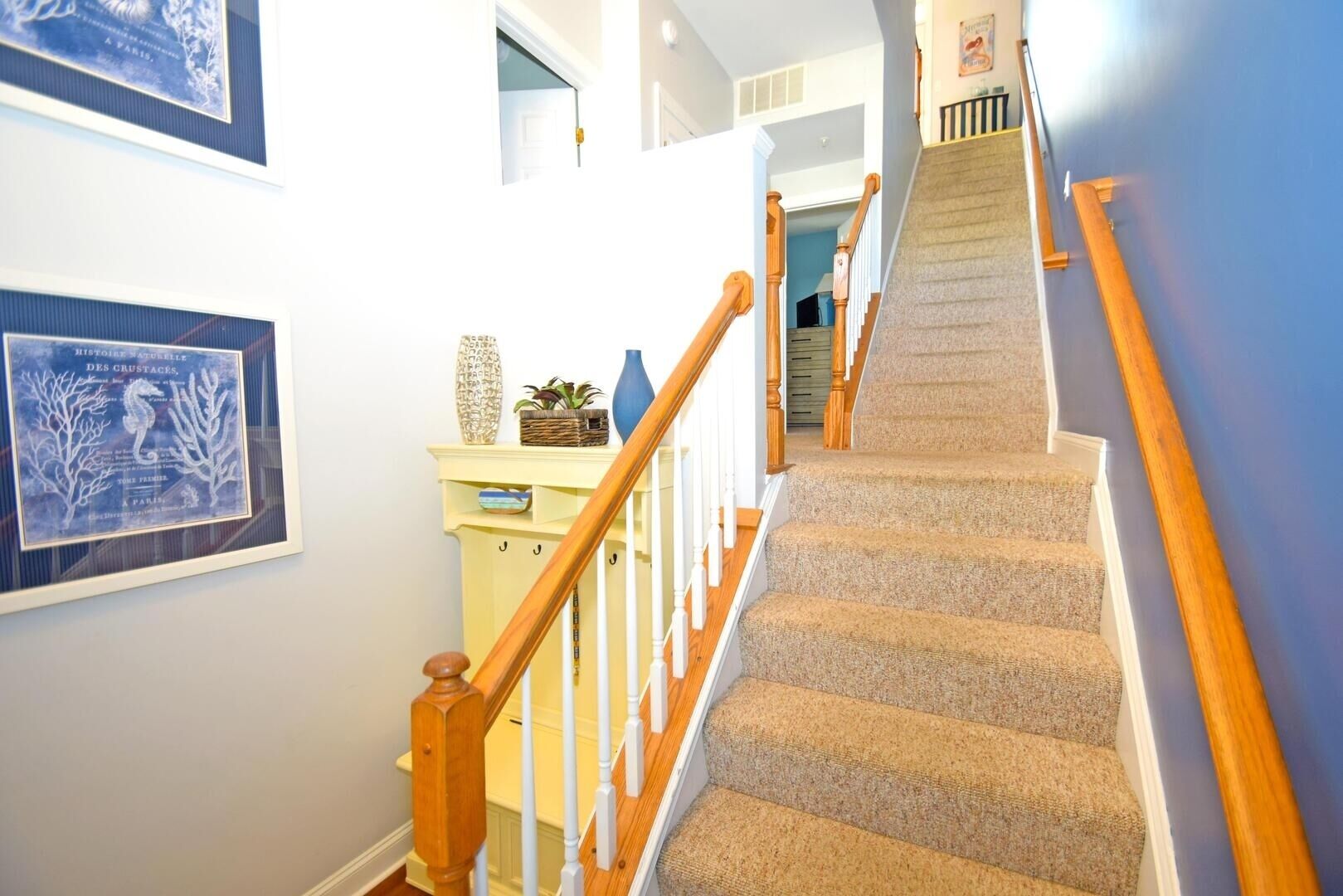 Una escalera con barandas de madera y peldaños alfombrados que sube a un piso superior.