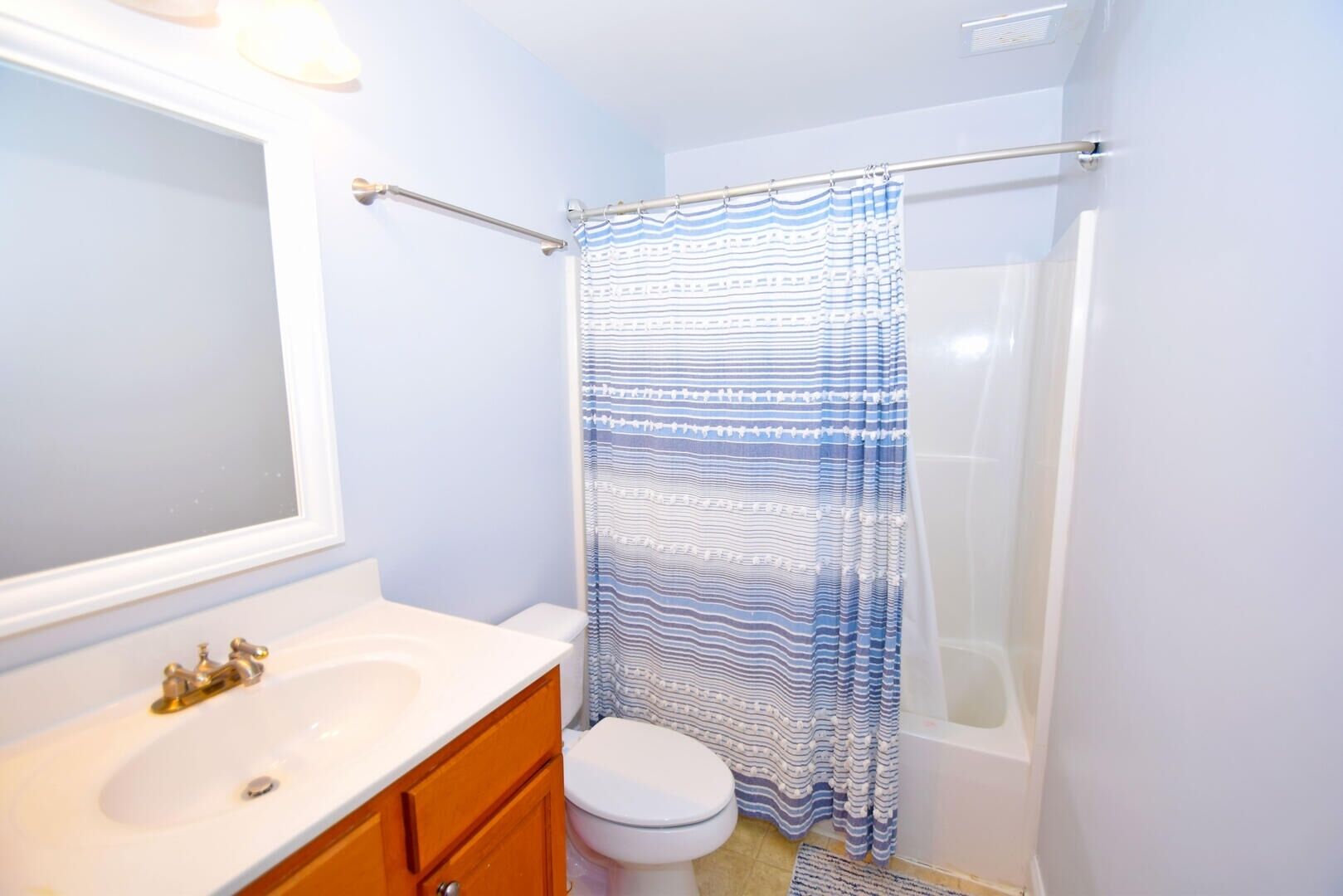 Un baño con un lavamanos blanco, un mueble de madera, un inodoro y una ducha con cortina a rayas azul y blanco.