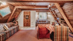 A cozy attic room with wooden beams, a loft bed, a sofa, and a window with curtains. - 54sl - Hot Tub - Pets Ok - Sleeps 4 2 Bedroom Cabin by RedAwning (Deming)