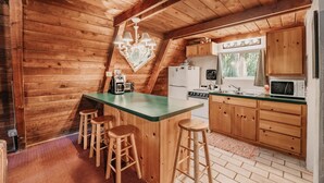 A cozy kitchen with wooden walls, a green island with stools, and basic appliances. - 54sl - Hot Tub - Pets Ok - Sleeps 4 2 Bedroom Cabin by RedAwning (Deming)
