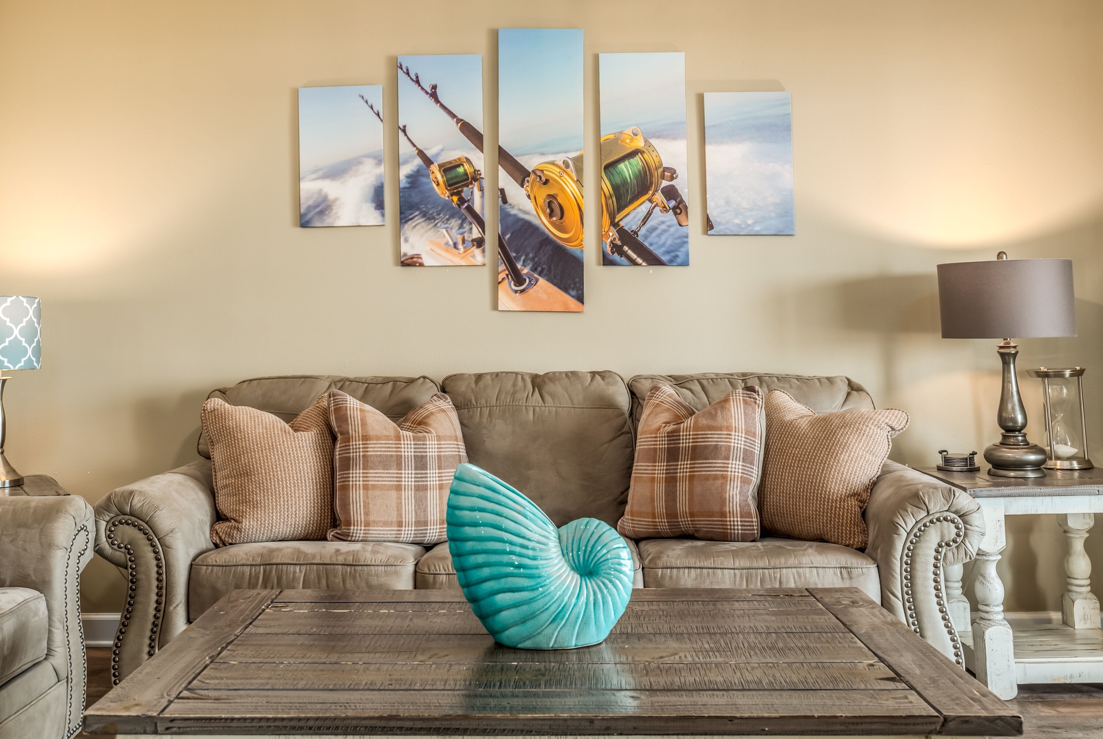 Un soggiorno con un divano beige, cuscini a quadri, un tavolino in legno e un quadro raffigurante una bobina da pesca appesa al muro.