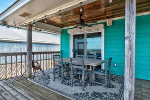 A covered outdoor area with a table and chairs, a ceiling fan, and a view of the ocean. - Chele's Bayside Cottage - 2304 Island Shores Dr 4 Bedroom Home by RedAwning (Dauphin Island)