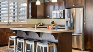 A modern kitchen with dark wood cabinets, stainless steel appliances, and a central island with bar stools. - Paradise Private Pool Retreat #17 6 Bedroom Home (Ivins)