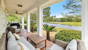 Une véranda aménagée avec des meubles en osier, une table en bois et une vue sur un lac et un terrain de golf.