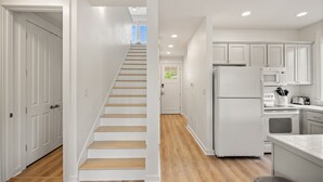 Une cuisine moderne avec des meubles blancs, un réfrigérateur, un four à micro-ondes et un escalier en bois menant à une autre pièce.