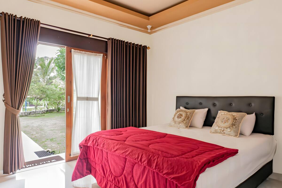 A bedroom with a bed, curtains, and a view of the outdoors.
