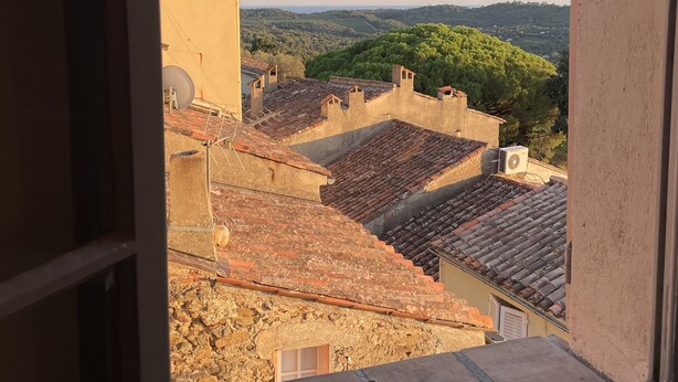 A view from a window overlooking a cityscape with terracotta rooftops and a distant green hill. - Maison de Village Avec vue Exceptionnelle, Presqu'île de Saint Tropez (Gassin)