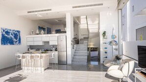 Une cuisine moderne avec des meubles blancs, un îlot central et des tabourets de bar. Un escalier mène à un niveau supérieur.