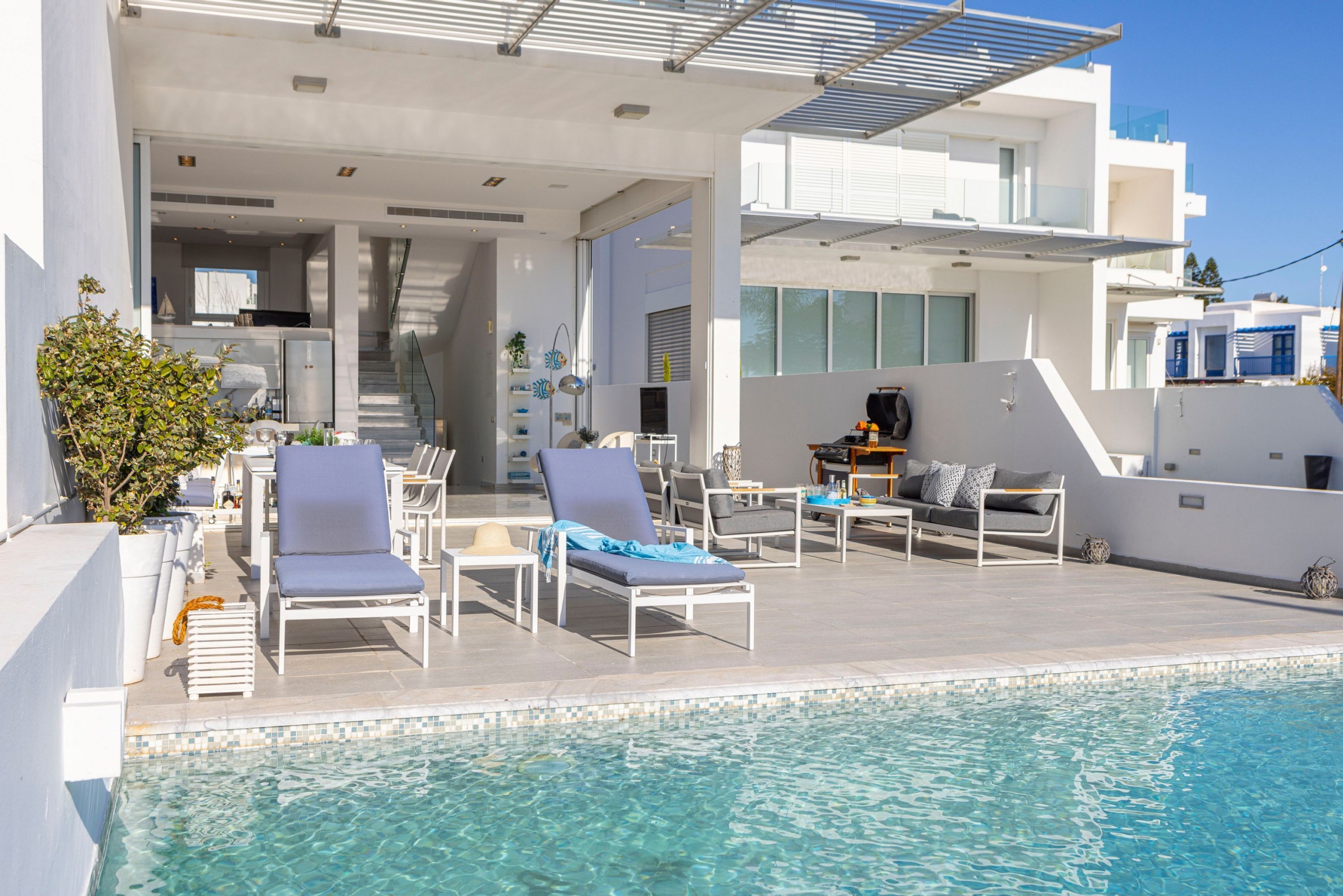 Un área moderna junto a la piscina con sillones de descanso y una zona de comedor.