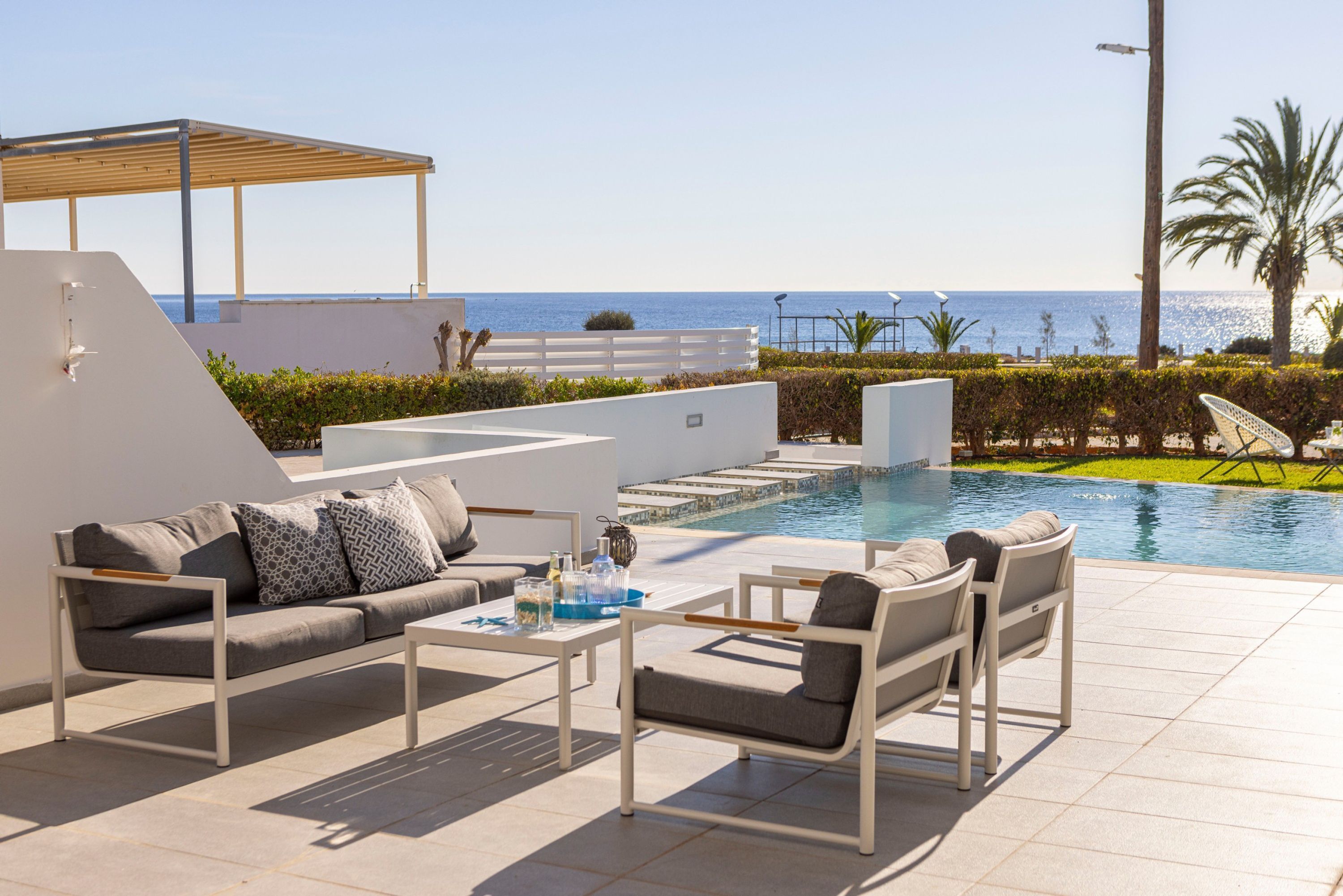 A modern outdoor lounge area with a pool, seating, and a view of the sea.