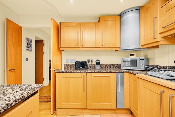A compact kitchen with wooden cabinets, a microwave, a toaster, and a dishwasher. - Morden2bed 2bath apartment Canary Wharf - upto 5ppl (London)
