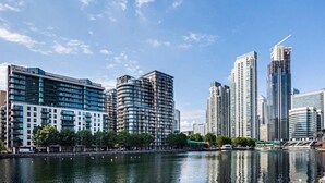 A waterfront cityscape with modern high-rise buildings, a river, and a clear sky. - Morden2bed 2bath apartment Canary Wharf - upto 5ppl (London)