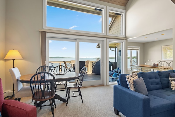 A spacious room with a dining area, a blue sofa, and large windows offering a view of the outdoors.