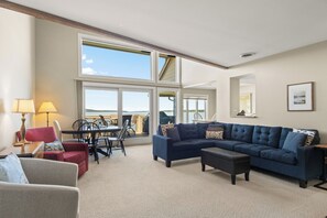 A spacious living area with a large window, a blue sofa, a red armchair, and a dining table with chairs.