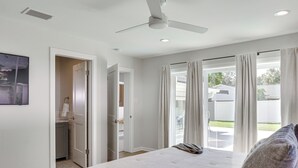 Une chambre dotée d’un grand lit, d’un ventilateur de plafond et offrant une vue sur le jardin arrière grâce à une porte-fenêtre coulissante.