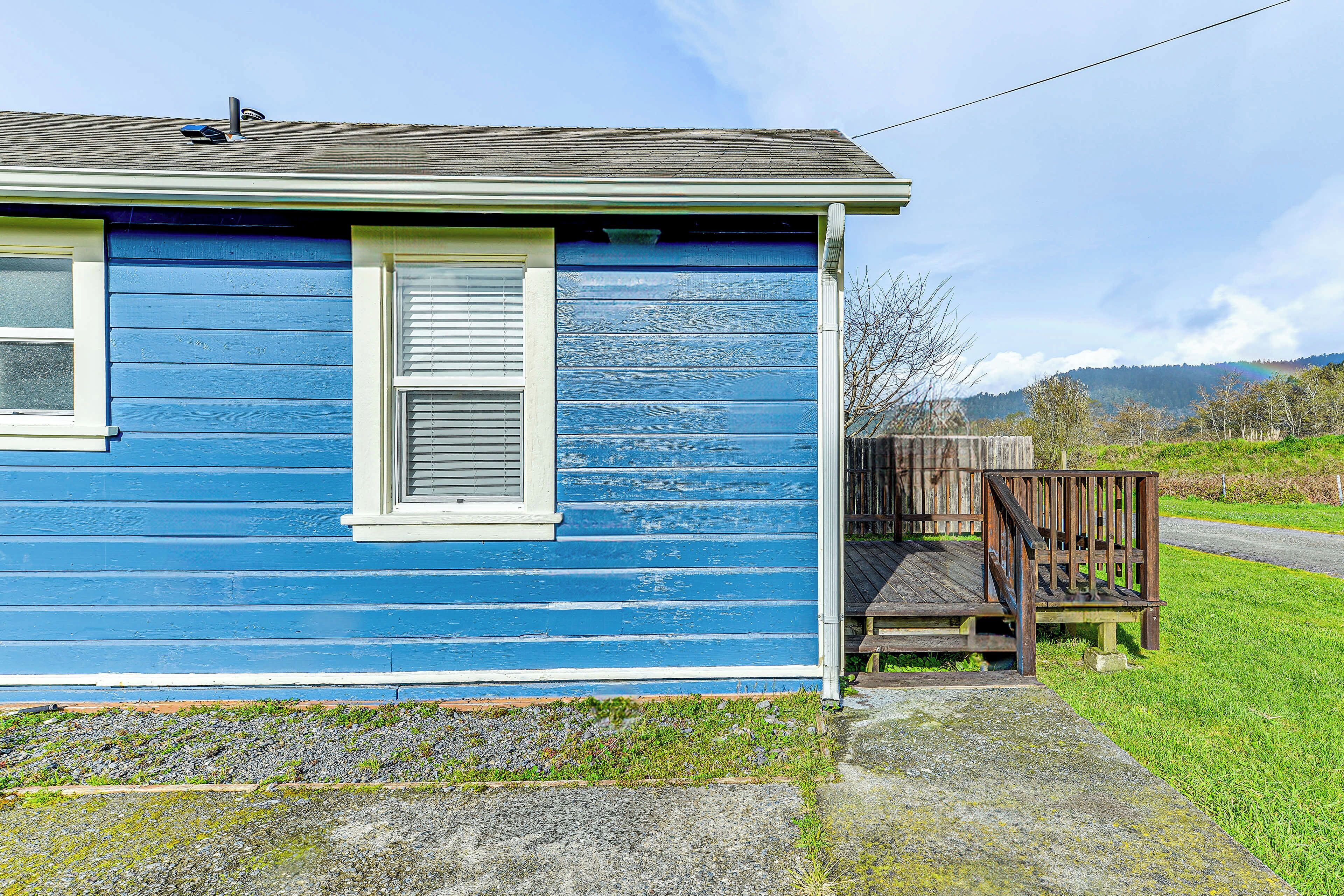 A blue house with a wooden deck and a window with shutters.