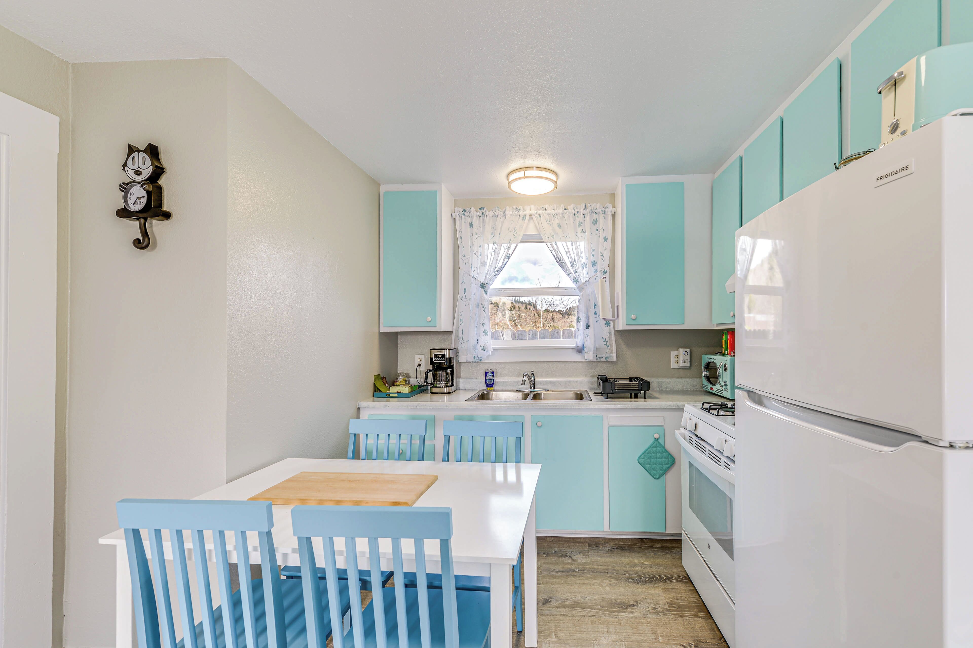 Une cuisine compacte avec des meubles de couleur turquoise, un réfrigérateur blanc et un coin repas avec des chaises bleues.