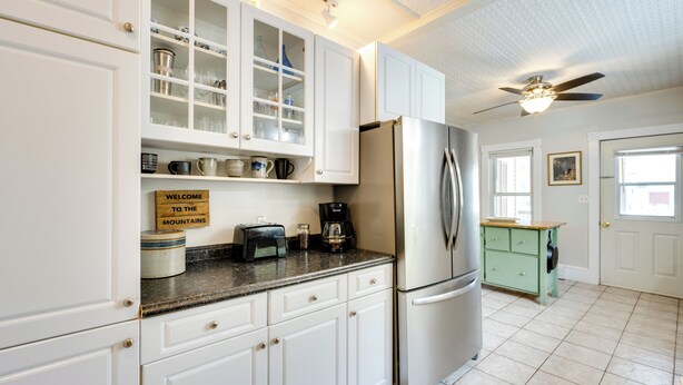 Una cocina con armarios blancos, un refrigerador de acero inoxidable, una cafetera y un tostador. Hay un letrero en la encimera que dice "BIENVENIDOS A LAS MONTAÑAS".