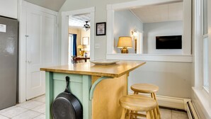 Una cocina con una isla de madera, dos taburetes, una estufa y una ventana con un televisor.