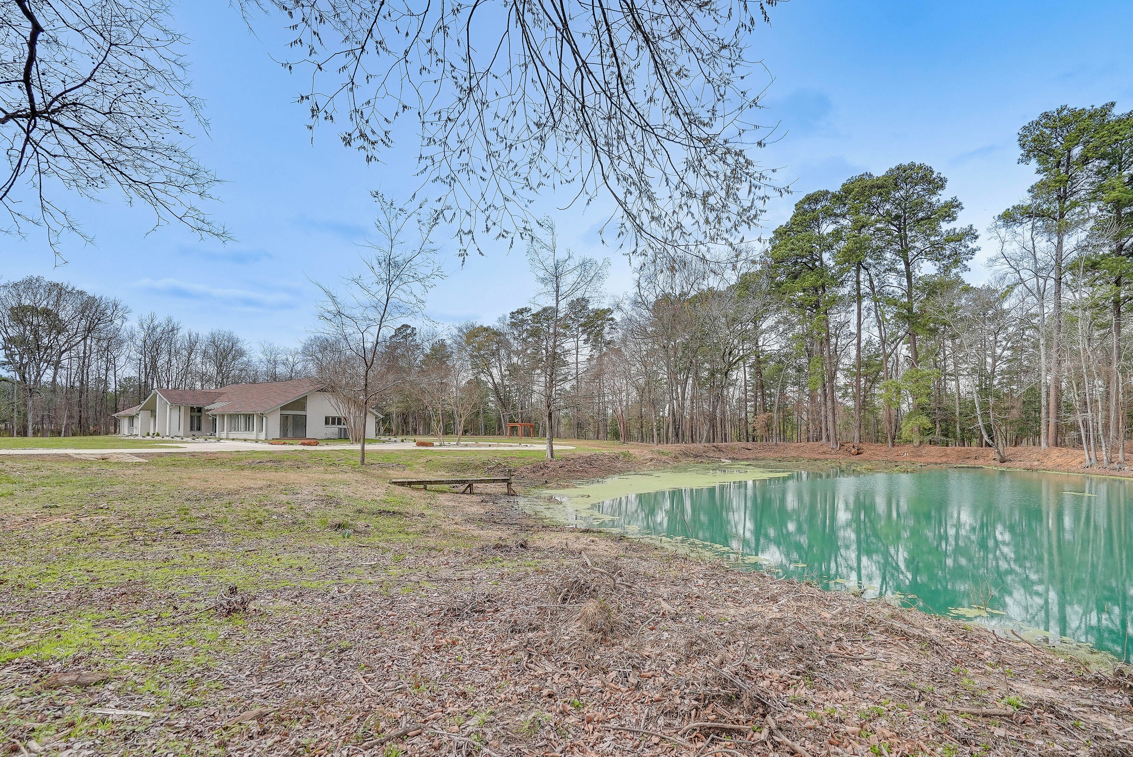 A house with a large yard, a pond, and surrounding trees.
