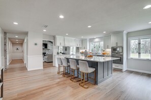 A modern kitchen with a central island, bar stools, stainless steel appliances, and a view of the outdoors. - Peaceful Longview Home w/ Pond, 6 Mi to Downtown! (Longview)