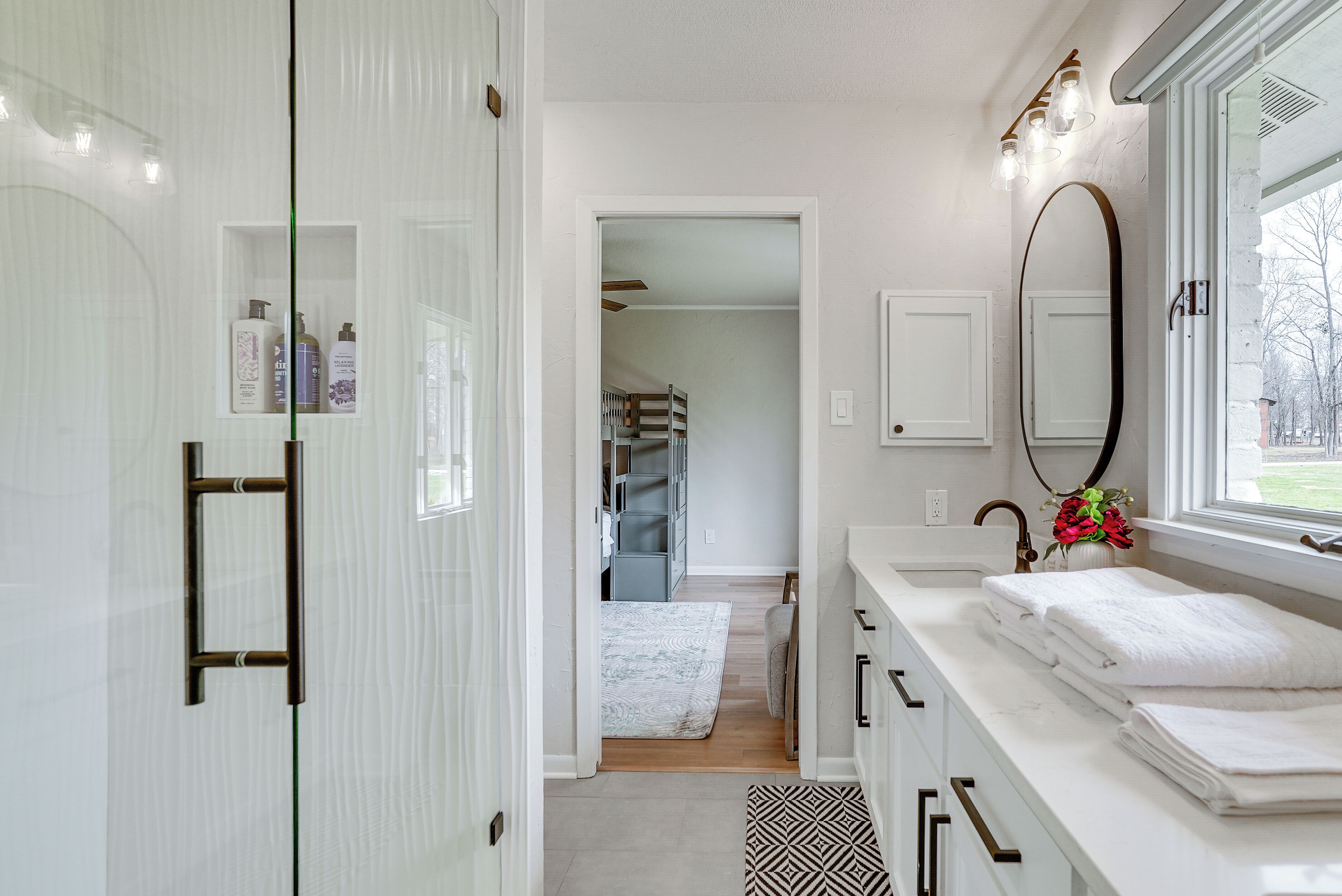 A modern bathroom with a walk-in shower, a vanity with a large mirror, and a window providing a view of the outdoors.