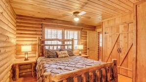 A log cabin bedroom with a wooden bed, two bedside tables, a ceiling fan, and a window with blinds. - Cropwell Cabin w/ Fire Pit, Near Logan Martin Lake (Cropwell)