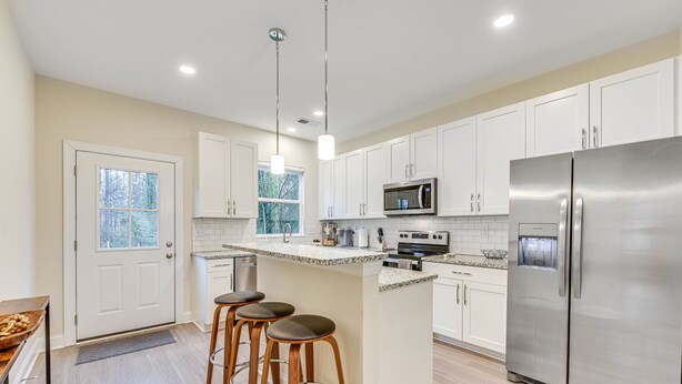 A modern kitchen with white cabinets, stainless steel appliances, and a central island with stools.