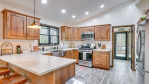 A modern kitchen with wooden cabinets, a large island with stools, stainless steel appliances, and a view to the outside.