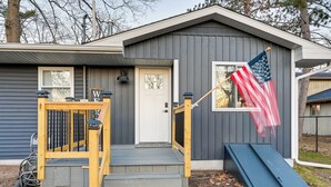 A house with a front porch, a sliding door, and a flagpole with an American flag. - Riverfront Michigan Cottage w/ Fire Pit & Kayaks! (Beaverton)